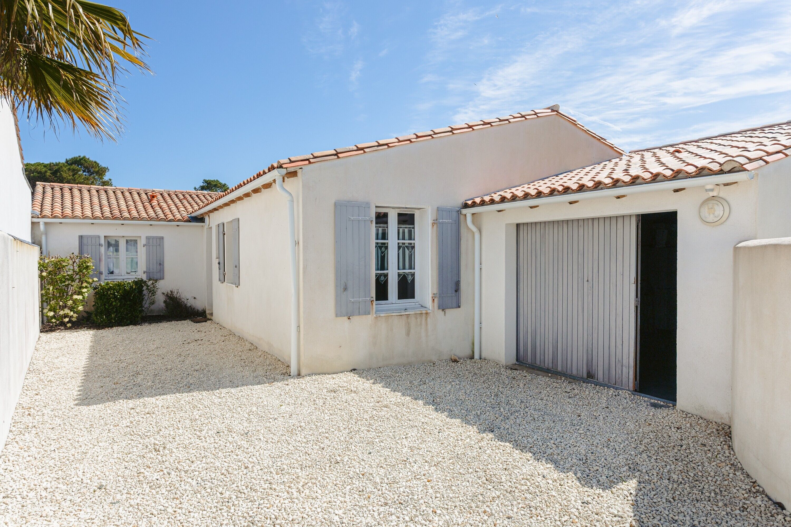 A building with a tiled roof, a gravel courtyard, and a garage door.