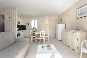 A modern kitchen with white appliances, a dining area with white chairs, and a grey sofa.