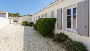 Un bâtiment avec une allée en gravier, des murs blancs et des volets gris.