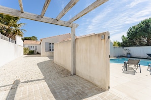 A covered outdoor area with a pool, a pergola, and a patio with chairs.