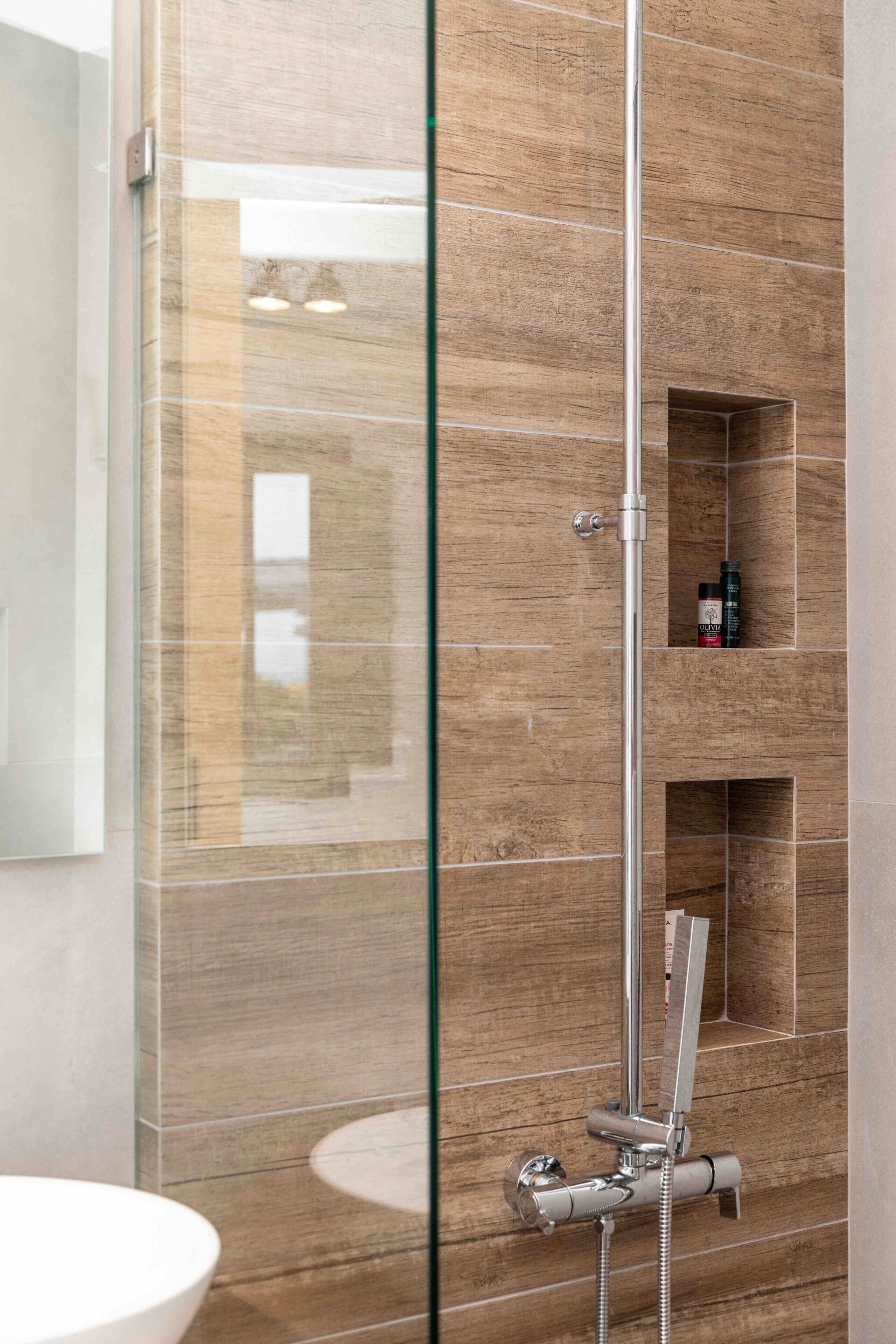 Une salle de bain moderne avec une douche à parois de verre, un lavabo blanc et des étagères intégrées pour le rangement.