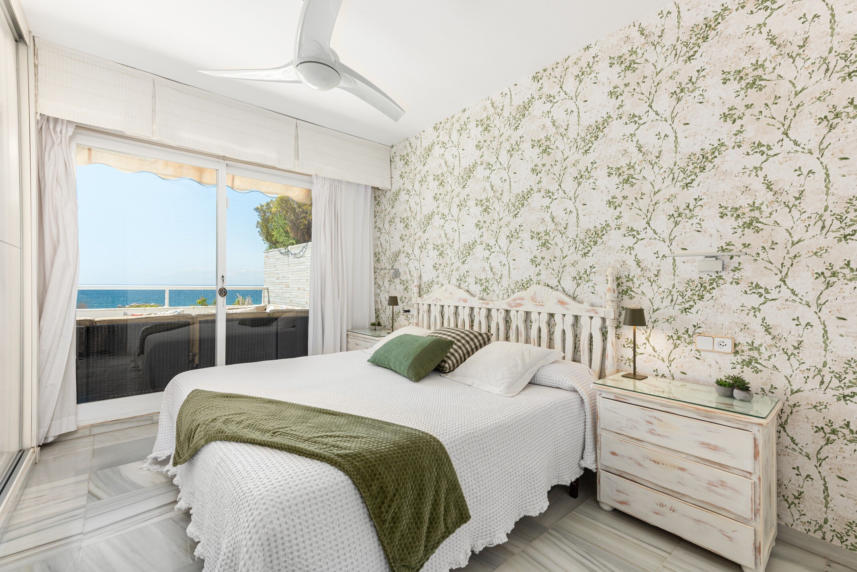Un dormitorio con cama, mesita de noche, cómoda y vista al mar.