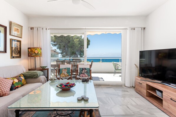 Un salon comprenant un canapé, un téléviseur, une table basse en verre et un balcon avec vue sur la mer.