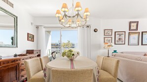 A dining area with a chandelier, wicker chairs, a table with a vase, a wooden sideboard, and a sofa. - Apartment 'Del Mar' with Sea View, Wi-Fi and Air Conditioning (Marbella)