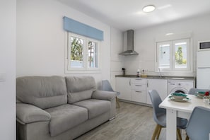 A modern kitchen with white cabinets, a grey sofa, and a dining table with chairs. - Apartment 'Atardecer' with Private Pool, Private Terrace and Wi-Fi (Conil de la Frontera)
