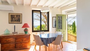 A dining area with a table and chairs, a wooden cabinet, a red lamp, and a window with a view. - Holiday Home 'Le Sophora' with Mountain View, Wi-Fi and Air Conditioning (ROCHEFORT DU GARD)