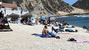 A beach with people sunbathing, umbrellas, and a building with a white facade.