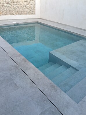 Ein rechteckiger Swimmingpool mit klarem Wasser, umgeben von einer gefliesten Terrasse und einer Steinmauer.