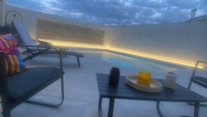 A rooftop terrace with lounge chairs, a small table with a tray, and a stone wall.
