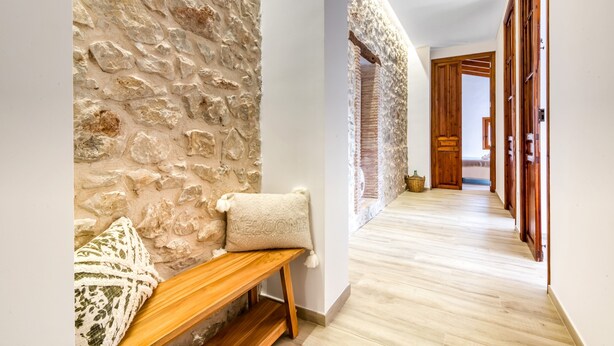 A hallway with a stone wall, wooden bench, and a welcome pillow.