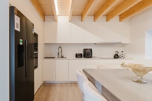 Une cuisine moderne avec des meubles blancs, un réfrigérateur noir, une machine à café et un vase en verre posé sur le plan de travail.