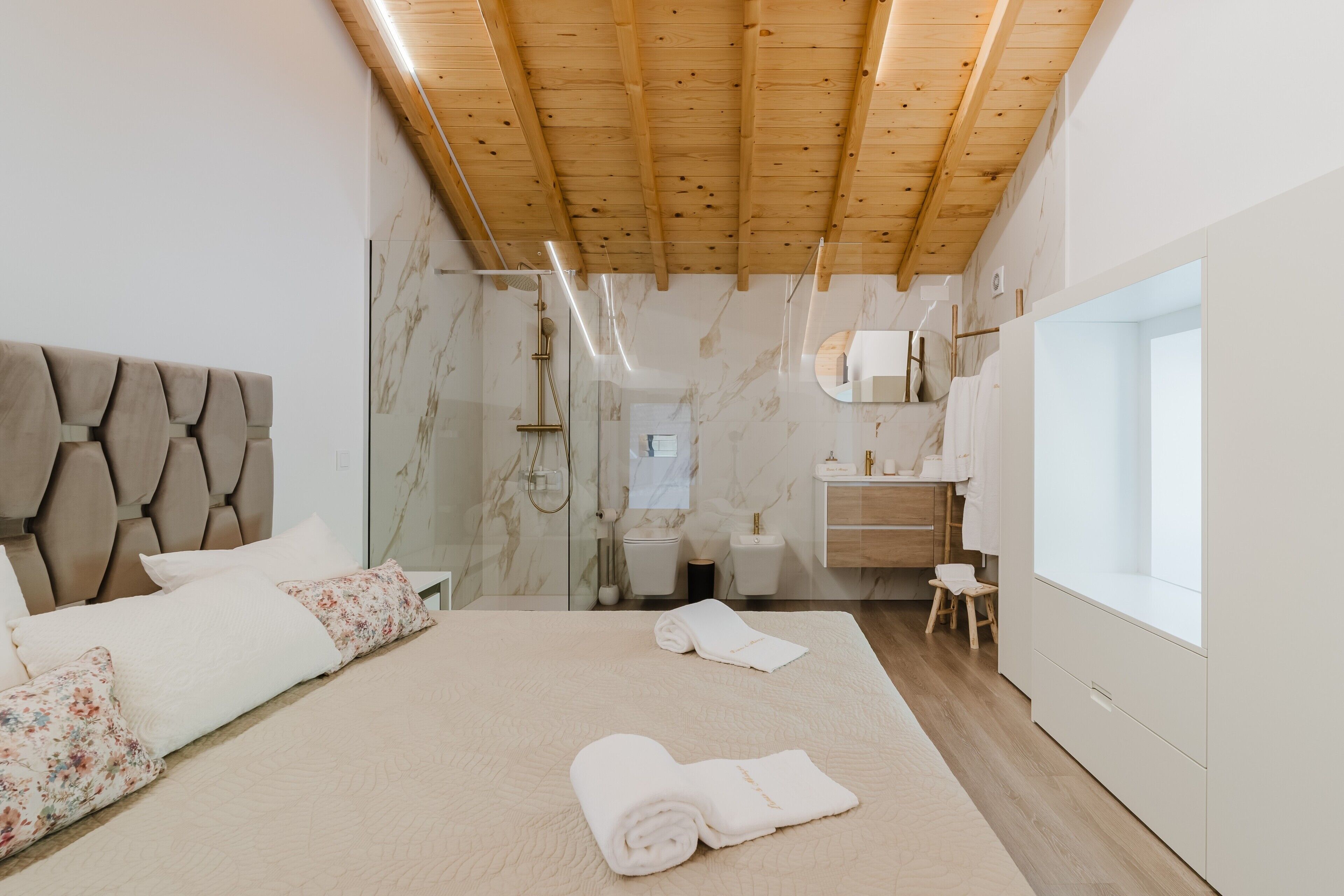 Un dormitorio con cama, techo de madera, baño con ducha y ventana.