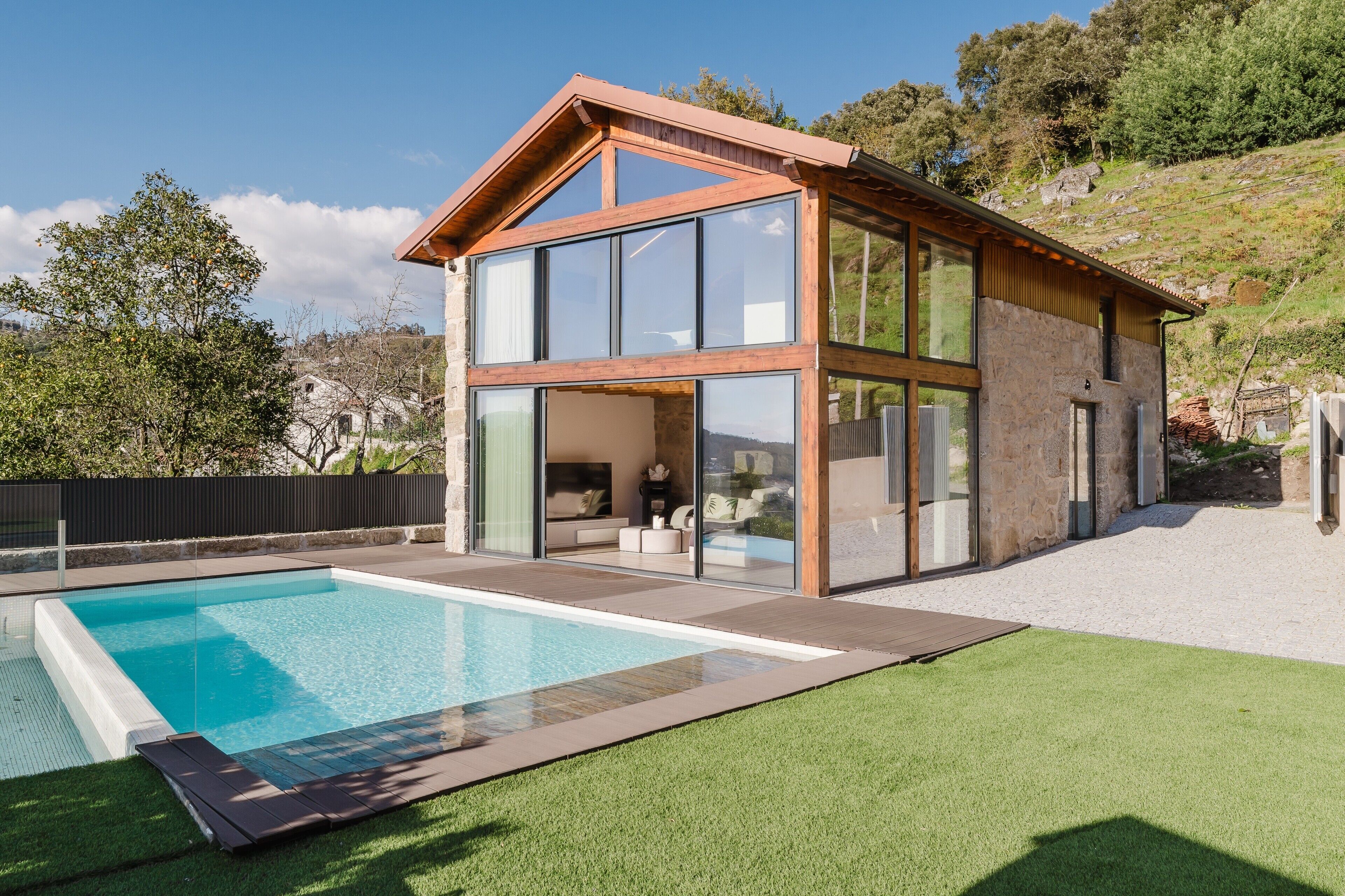 A modern house with a swimming pool, large windows, and a stone exterior.