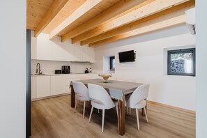 Une cuisine moderne avec des meubles blancs, un plafond en bois et une table à manger avec quatre chaises.