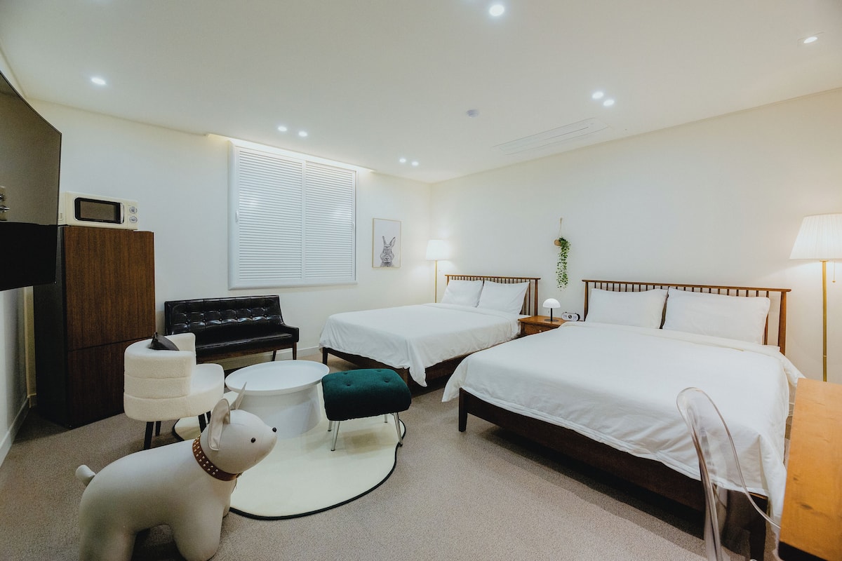 A bedroom with two beds, a desk, a chair, a small round table, and a decorative dog statue.
