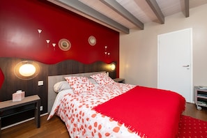 Une chambre à coucher avec un lit, des tables de chevet, une commode, un mur rouge et une porte.