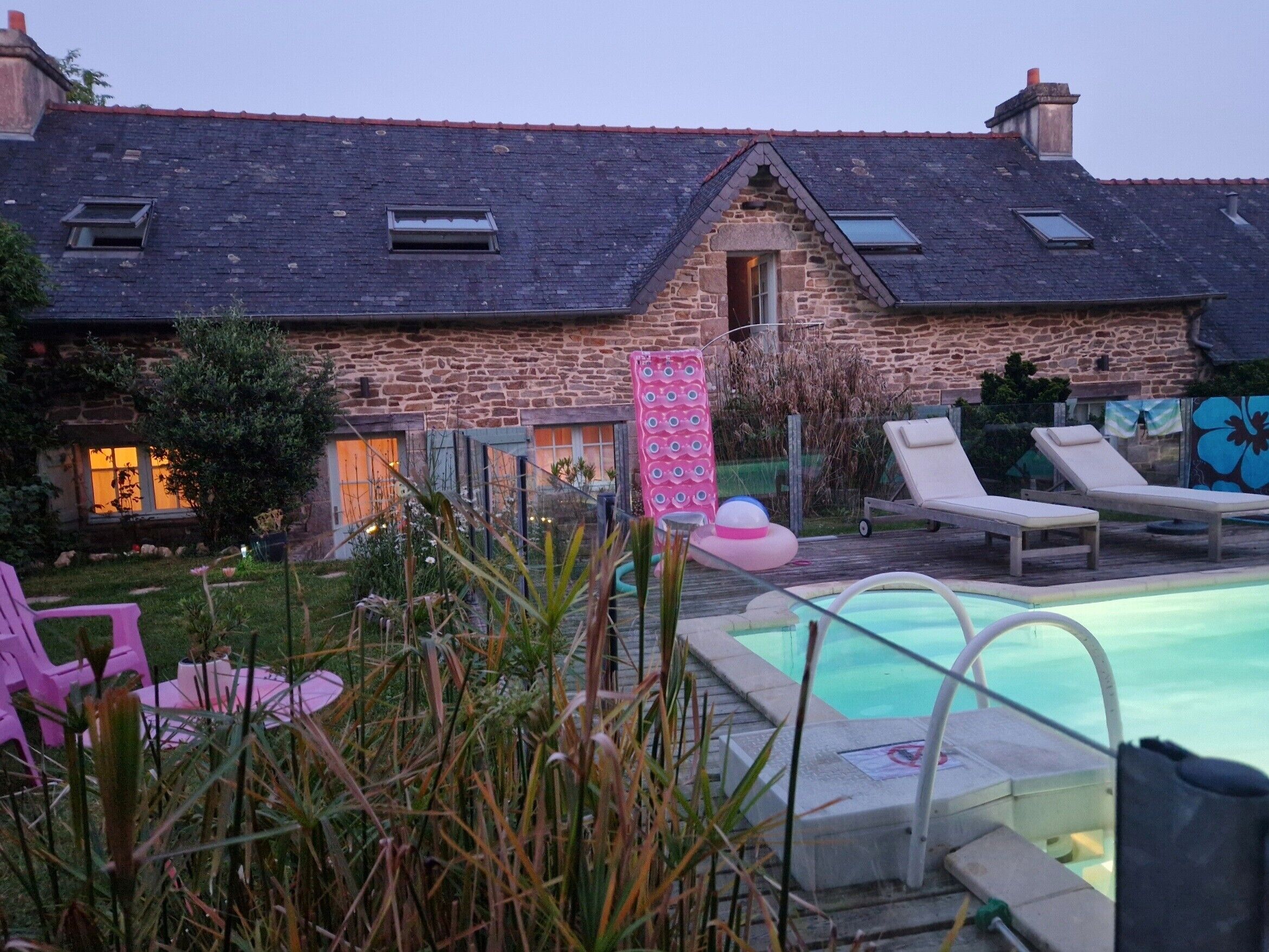 A stone building with a swimming pool, lounge chairs, and a pink inflatable pool float.