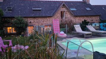 A stone building with a swimming pool, lounge chairs, and a pink inflatable pool float.