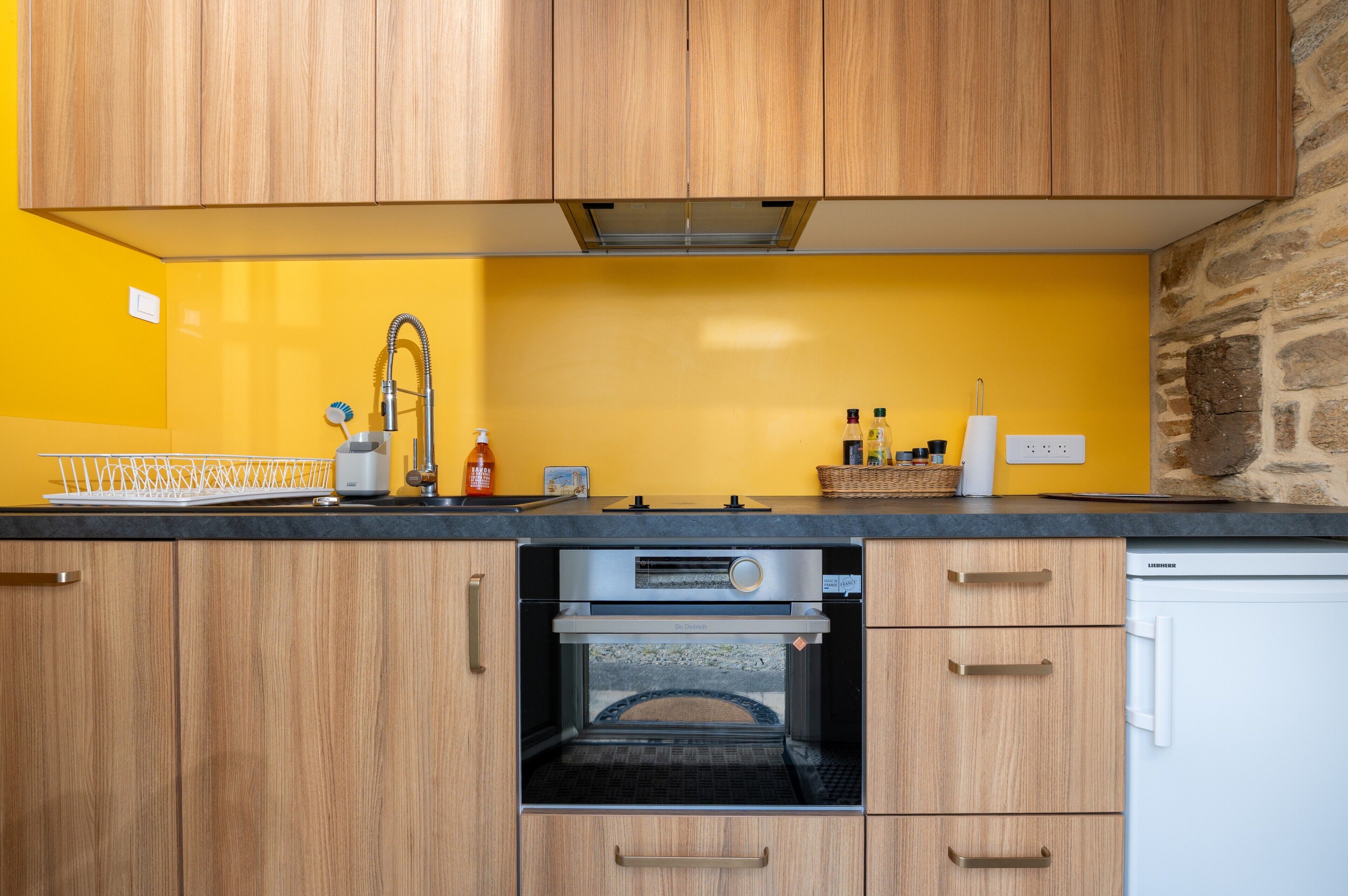 Eine Küche mit Holzausstattung, einem Backofen, einer Spüle und einer gelben Rückwand.