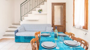 Comedor con mesa lista para cuatro personas, un sofá, una escalera y una puerta.