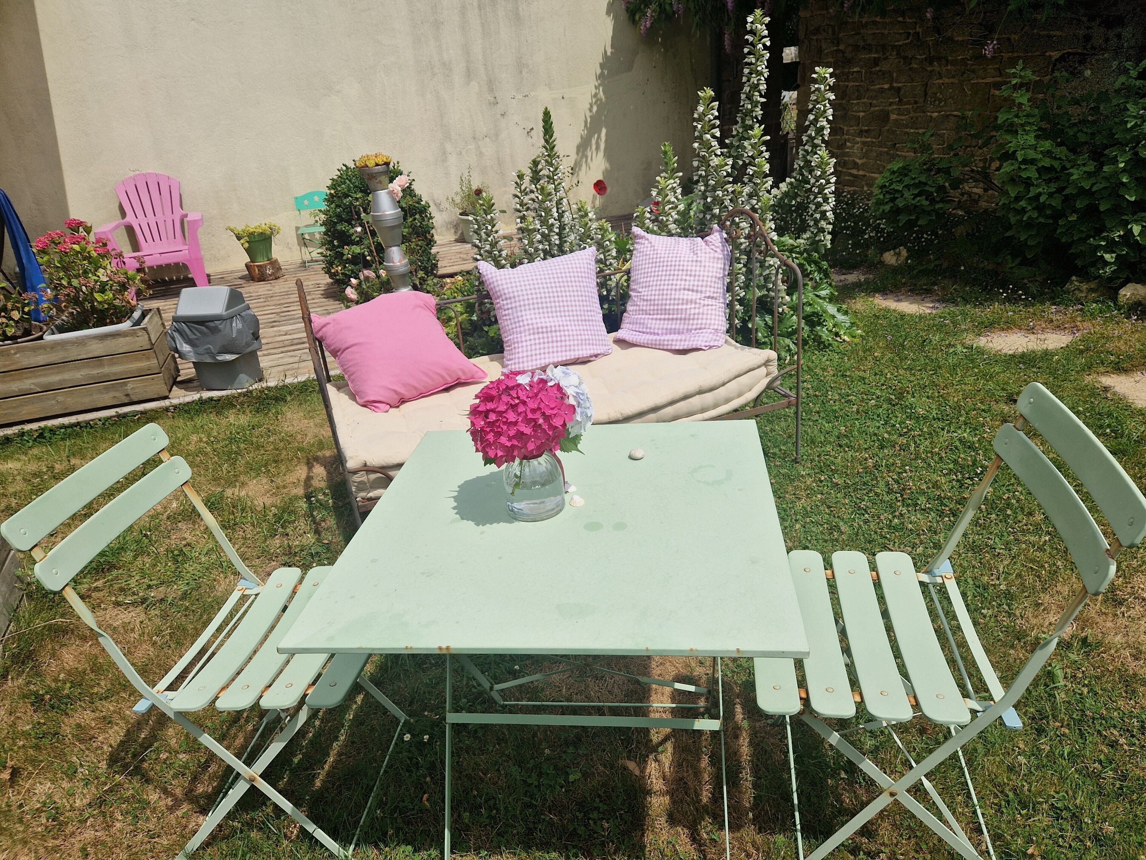 A patio with a table and chairs, a cushioned bench with pillows, and potted plants.
