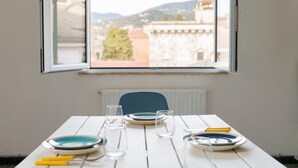 A dining table with plates, glasses, and cutlery, a chair, and a window with a view of buildings and hills.