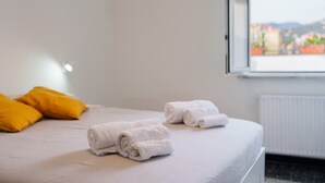 A hotel room with a bed, two rolled towels, a window with a view, and a radiator.