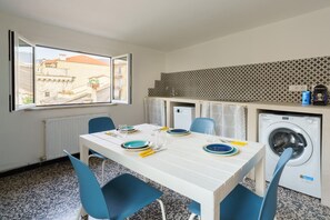 Habitación pequeña con mesa de comedor para dos, lavadora y vista a la calle a través de una ventana.