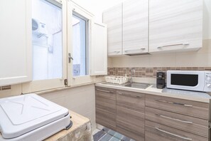 Uma cozinha compacta com armários brancos, micro-ondas e uma janela com unidade de ar condicionado.