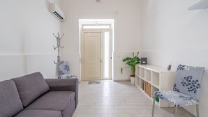 A modern living room with a grey sofa, a patterned armchair, a coat rack, and a potted plant. - Apartment 'Dafne Home' with Wi-Fi and Air Conditioning (Siracusa)
