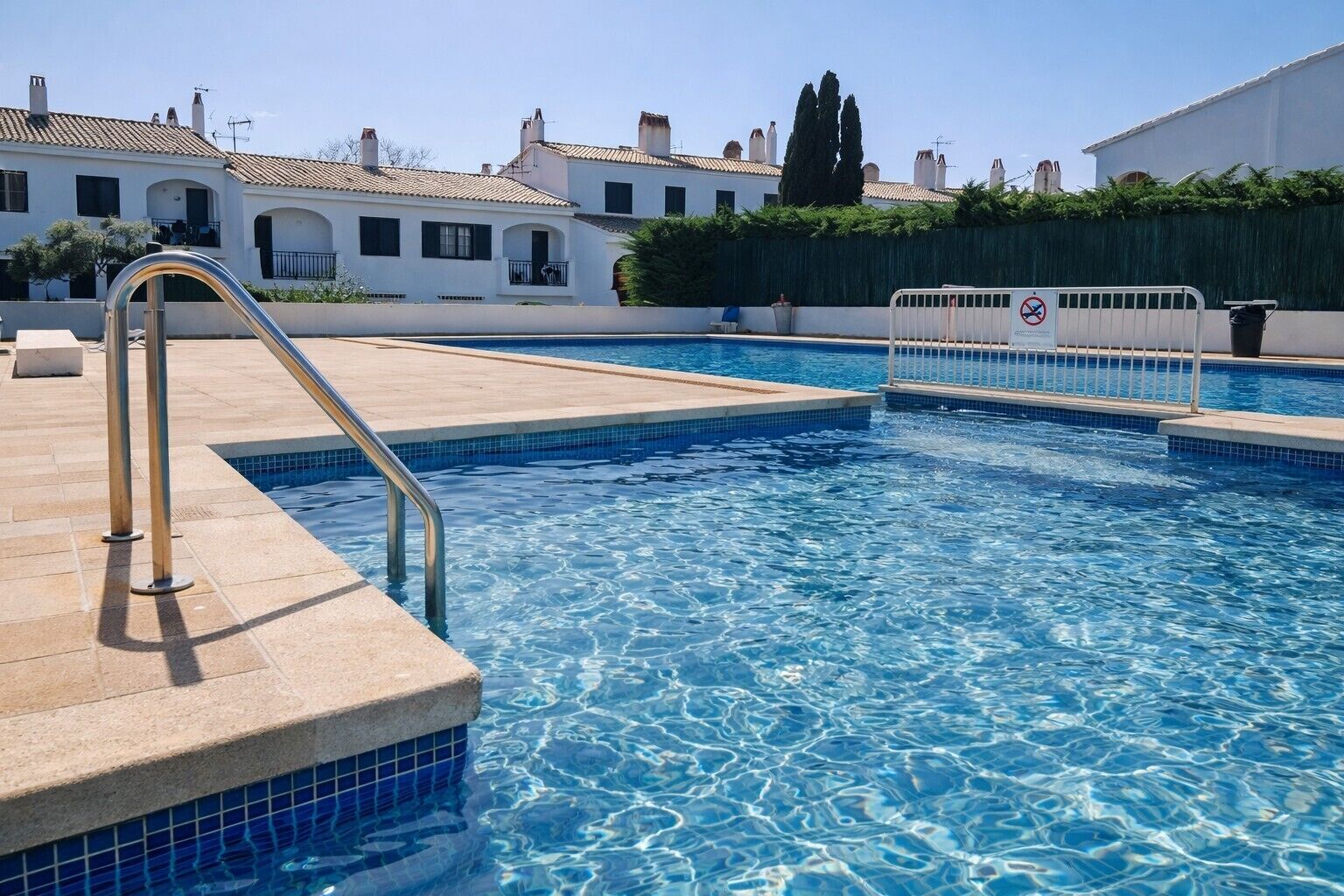 Una piscina con una scala metallica, gradini piastrellati e un segnale che indica divieto di balneazione.