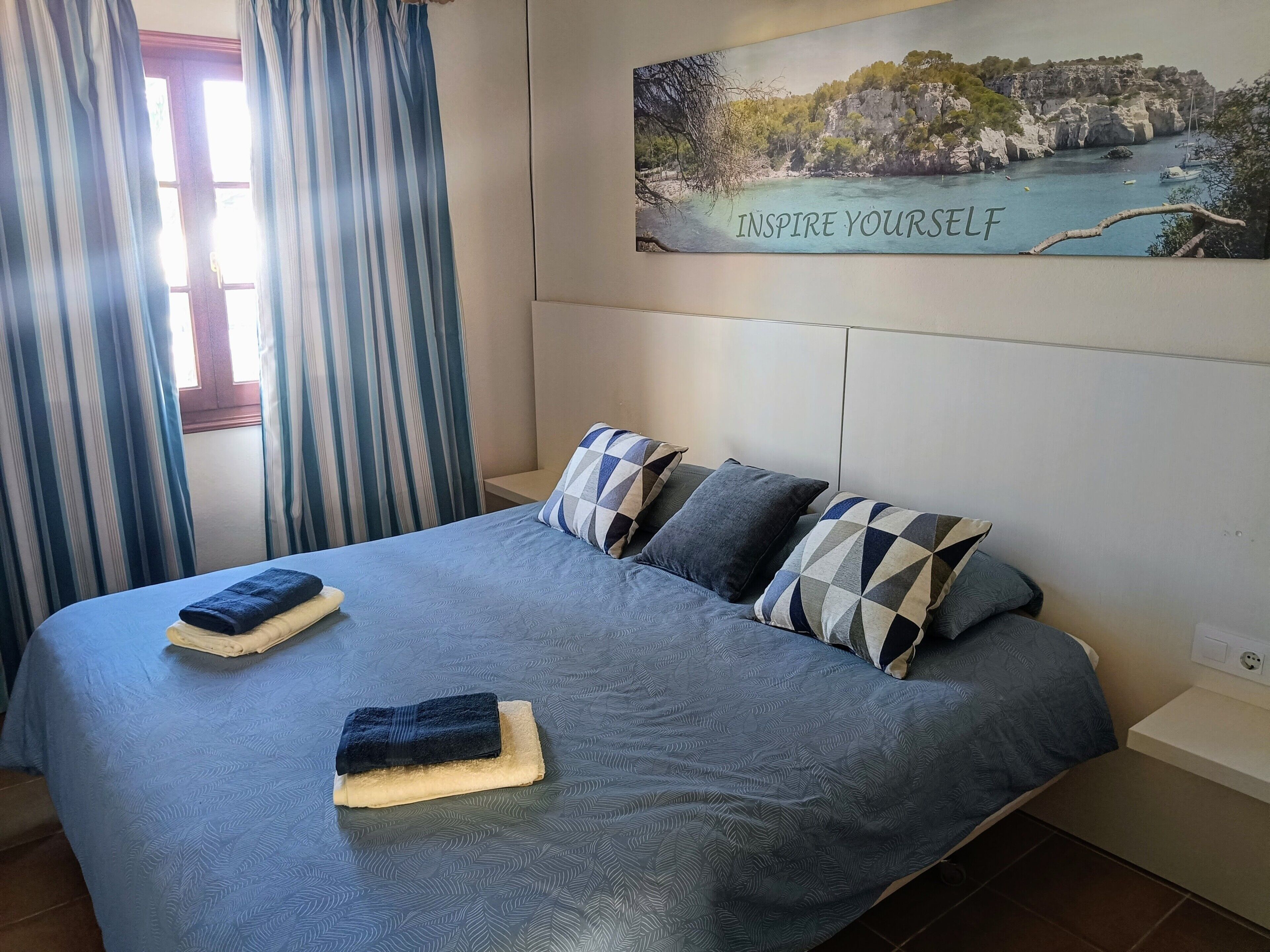 Un letto con una coperta blu a motivi, cuscini e asciugamani piegati.