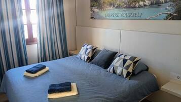 Un letto con una coperta blu a motivi, cuscini e asciugamani piegati.