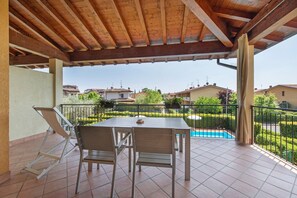 A covered patio with a table and chairs, a pool, and a view of houses.