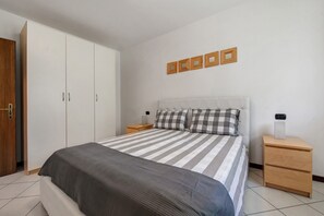 A bedroom with a bed, a wardrobe, a nightstand, and a wall-mounted light fixture.