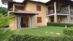 Uma casa de dois andares com varanda, alpendre e gramado bem cuidado.