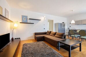 Una sala de estar moderna con un sofá modular, un televisor de pantalla plana, una mesa de centro y una cocina al fondo.