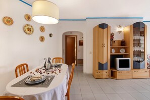 Spiseområde med et bord dækket til to, et fjernsyn og et skab med drikkeglas.