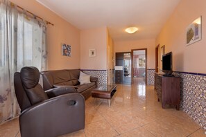 A living room with a sofa, a coffee table, a TV, and a kitchen area in the background.