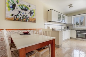 Une cuisine avec des meubles blancs, une cuisinière et une table à manger avec des chaises.