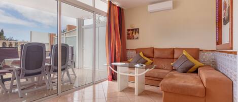 Una sala de estar con un sofá, sillas, una mesa de centro y un ventanal de vidrio que da a un espacio exterior.