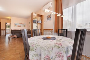 Un comedor con una mesa redonda, sillas, un candelabro central y vistas a través de amplios ventanales.