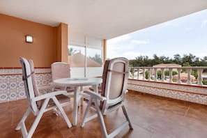 Un balcon avec une table et des chaises, un sol carrelé et une vue sur des immeubles et des arbres.