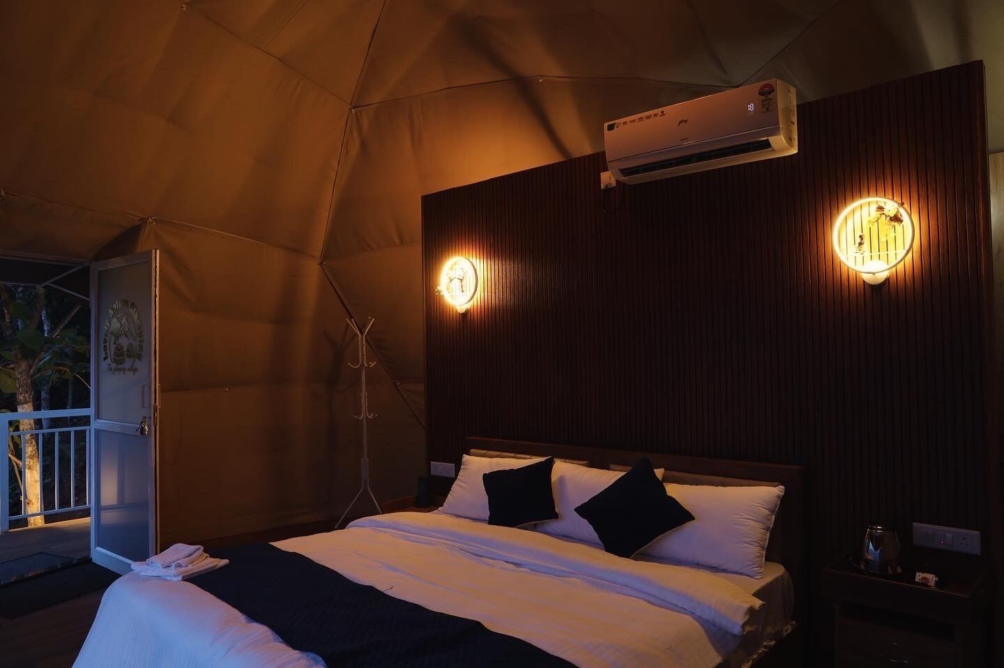 A tent-style room with a bed, two wall-mounted lights, an air conditioning unit, and a coat rack.