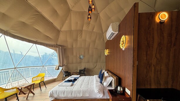 A cozy bedroom with a large bed, wooden furniture, a small table, and a view through a large window. - Domestay with Mountain View - Gateway of Munnar (Munnar)