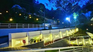 A well-lit outdoor area with a series of steps leading up to a white railing, surrounded by potted plants and trees. - Domestay with Mountain View - Gateway of Munnar (Munnar)