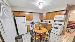 Cocina pequeña con armarios de madera, un refrigerador blanco, una estufa y una mesa de comedor con sillas.