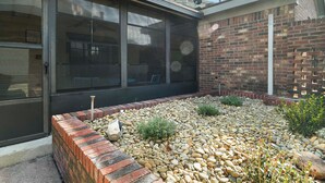 A brick exterior with a glass door and windows, a gravel pathway, and a small garden area with plants.