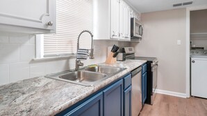 A kitchen with a granite countertop, white cabinets, a built-in microwave, and a dishwasher.