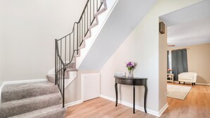 A staircase with carpeted steps and a metal railing, leading to a room with a wooden floor and a small table with a vase of flowers.